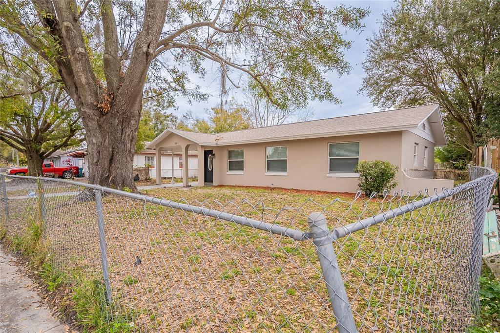 A beige single-story house with a chain-link fence and a large tree in the yard — 1335 LESCOT LANE, ORLANDO, FL