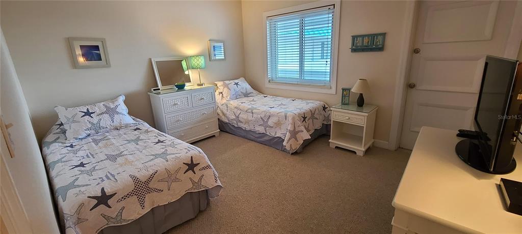 A bedroom features two twin beds with starfish-patterned quilts, a dresser, and a television — 815 OCEAN SHORE BOULEVARD UNIT 12A, ORMOND BEACH, FL