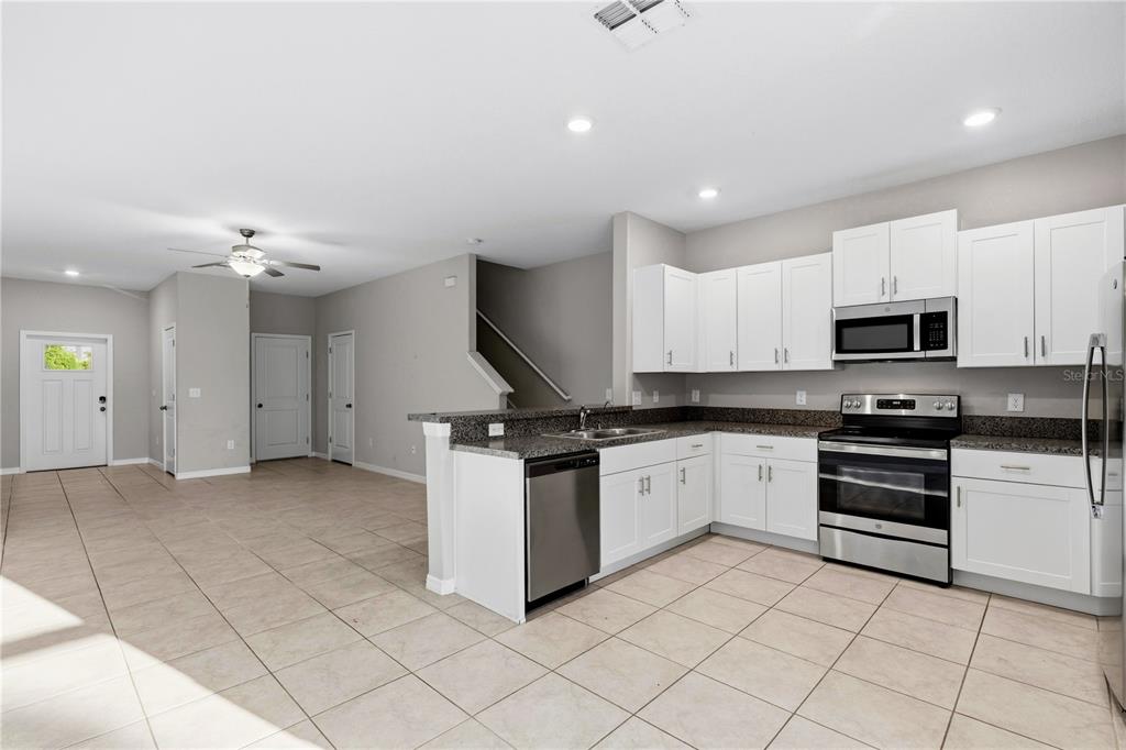 A kitchen with white cabinets and stainless steel appliances overlooks an open living area — 3527 BELLMEADE COURT, WESLEY CHAPEL, FL