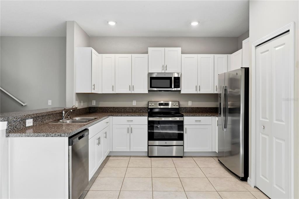 A kitchen features white cabinets, stainless steel appliances, and granite countertops over tile flooring — 3527 BELLMEADE COURT, WESLEY CHAPEL, FL
