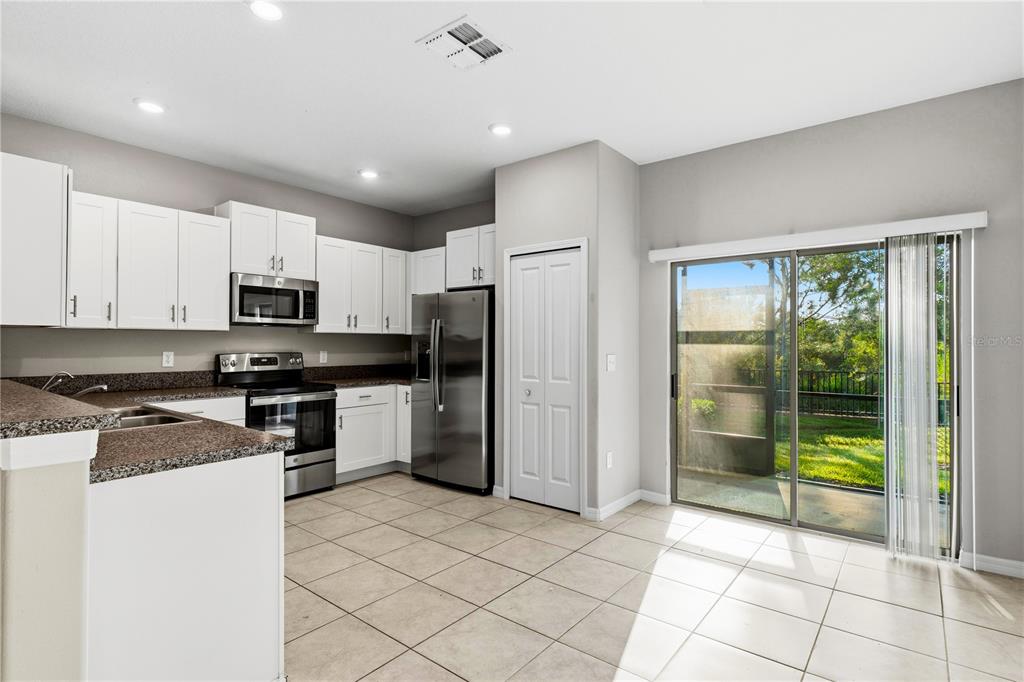 A kitchen with white cabinets, stainless steel appliances, granite countertops, and a sliding glass door — 3527 BELLMEADE COURT, WESLEY CHAPEL, FL