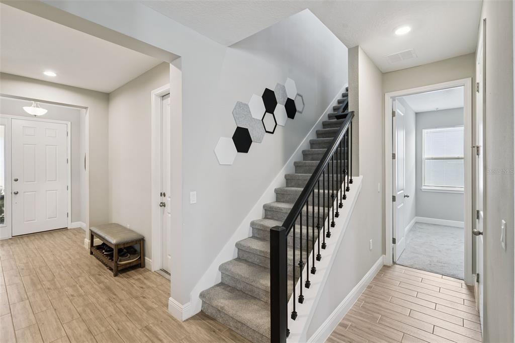 An entryway features wood-look tile flooring, a carpeted staircase with a black railing, and wall decor — 4442 LIONS GATE DRIVE, CLERMONT, FL