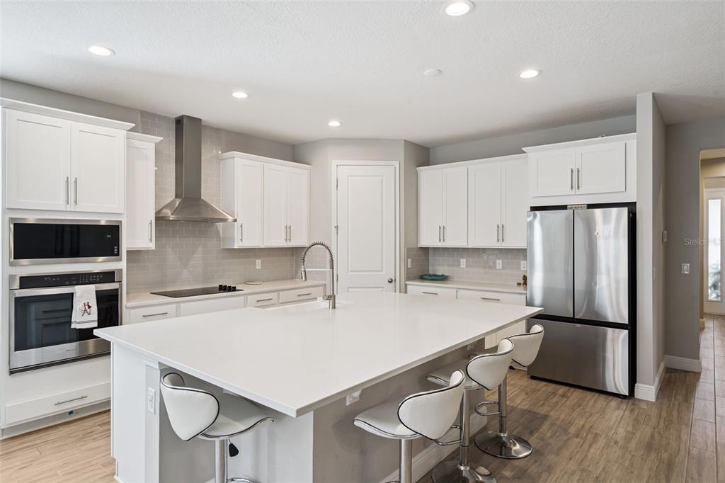A modern kitchen features white cabinetry, stainless steel appliances, a large island, and wood-look flooring — 4442 LIONS GATE DRIVE, CLERMONT, FL