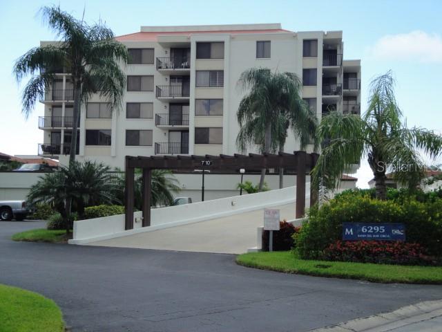 A multi-story apartment building with a parking garage entrance and palm trees in the foreground — 6295 BAHIA DEL MAR CIRCLE UNIT 216, ST PETERSBURG, FL