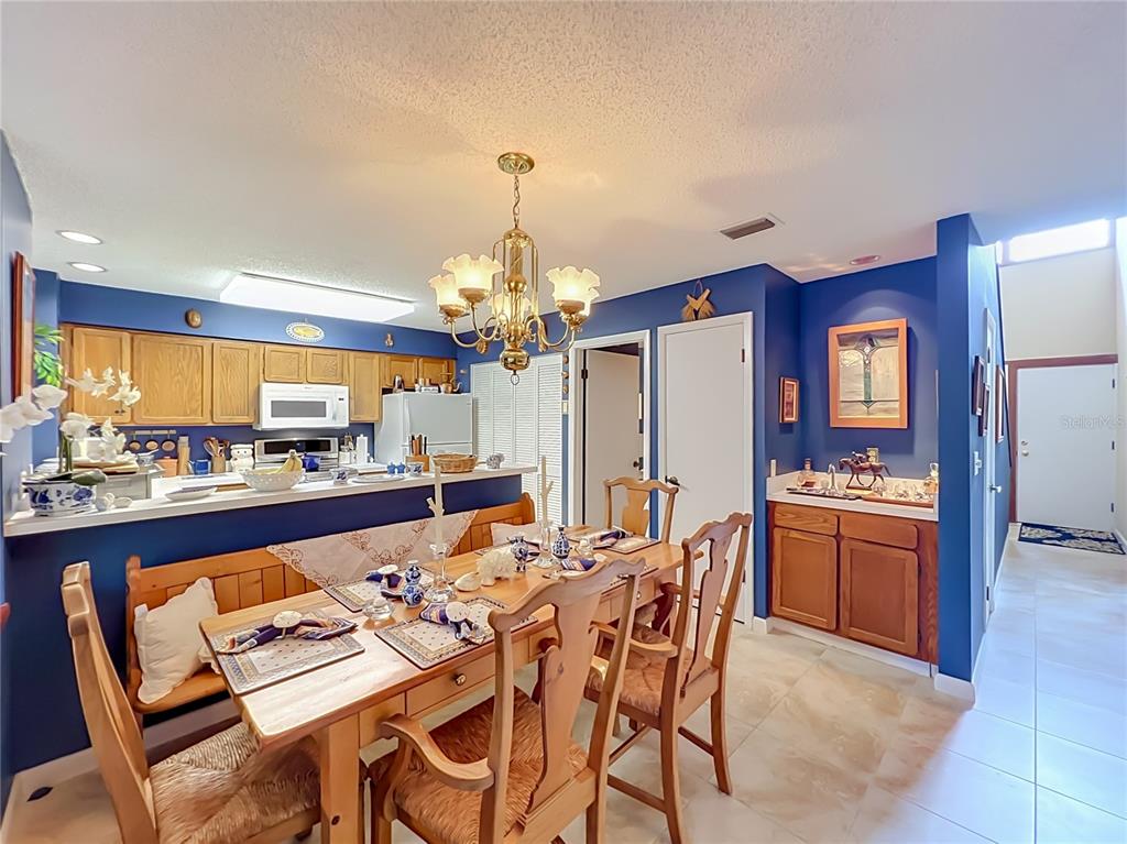 A dining area with a wooden table and chairs sits before a blue-walled kitchen — 2184 WOODBRIDGE ROAD UNIT 2184, LONGWOOD, FL
