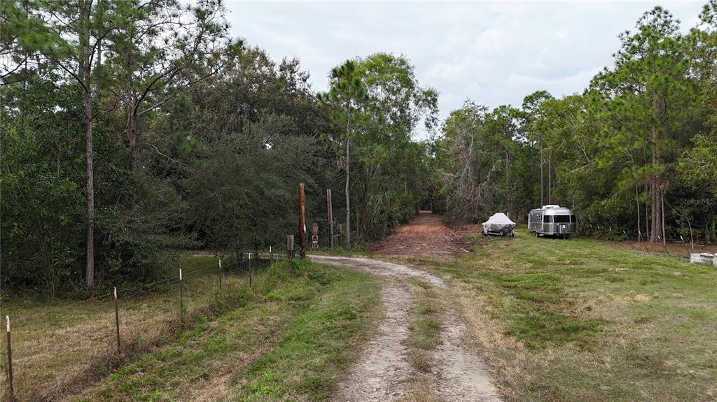 A dirt driveway leads through a wooded area with a parked trailer and boat — PANTERA LN, NAPLES, FL