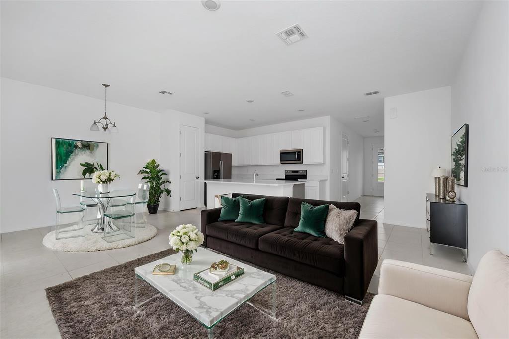 An open-concept living room and kitchen featuring white cabinetry, a dark sofa, and tile flooring — 1526 DISCOVERY STREET, DAVENPORT, FL