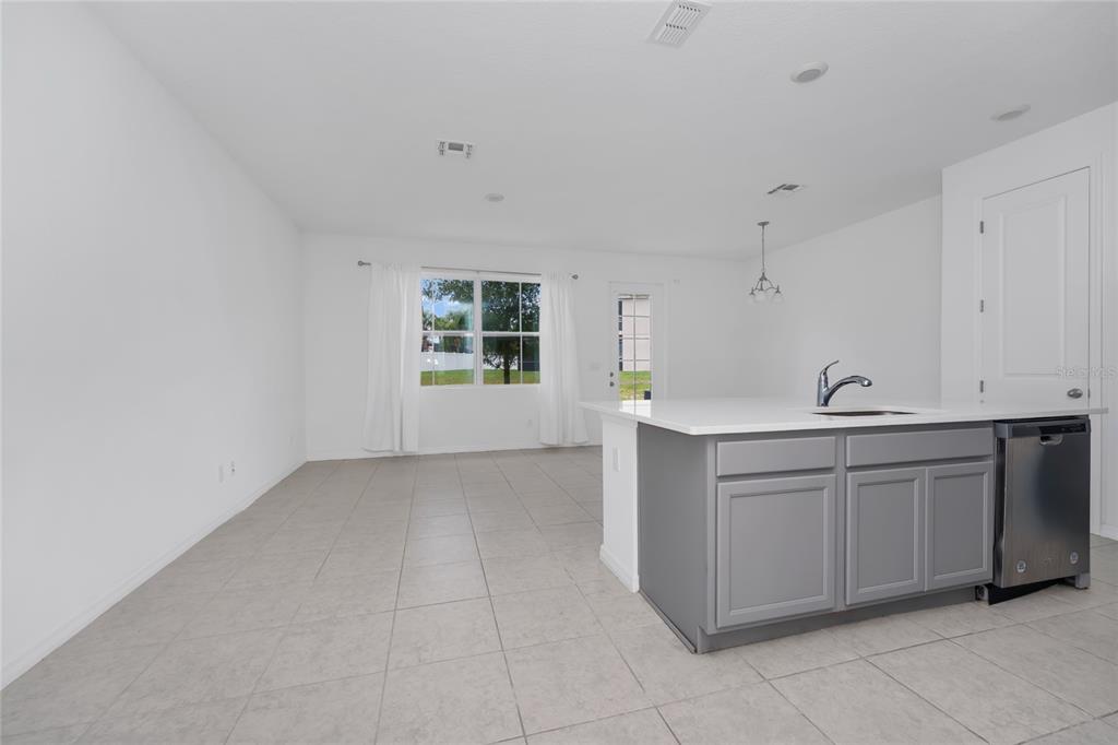 A kitchen island with gray cabinets and a stainless steel dishwasher faces an open living area — 1526 DISCOVERY STREET, DAVENPORT, FL