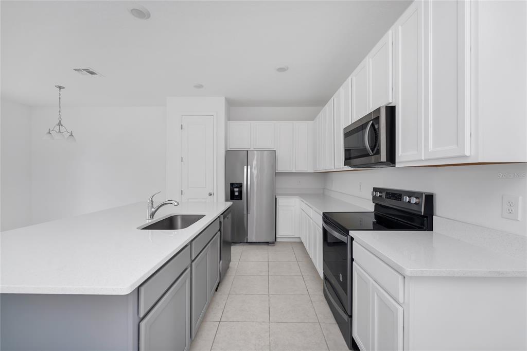 A modern kitchen features white cabinets, gray island cabinetry, stainless steel appliances, and quartz countertops — 1526 DISCOVERY STREET, DAVENPORT, FL