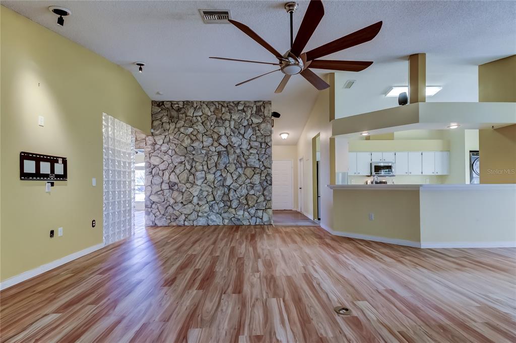 A living room with wood-look flooring, a stone accent wall, and a ceiling fan — 1795 BAYHILL DRIVE, OLDSMAR, FL