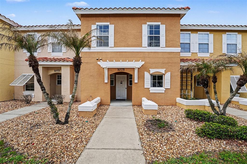 The exterior of a two-story tan stucco townhouse features a central entrance and palm trees — 1081 PARK RIDGE CIRCLE, KISSIMMEE, FL