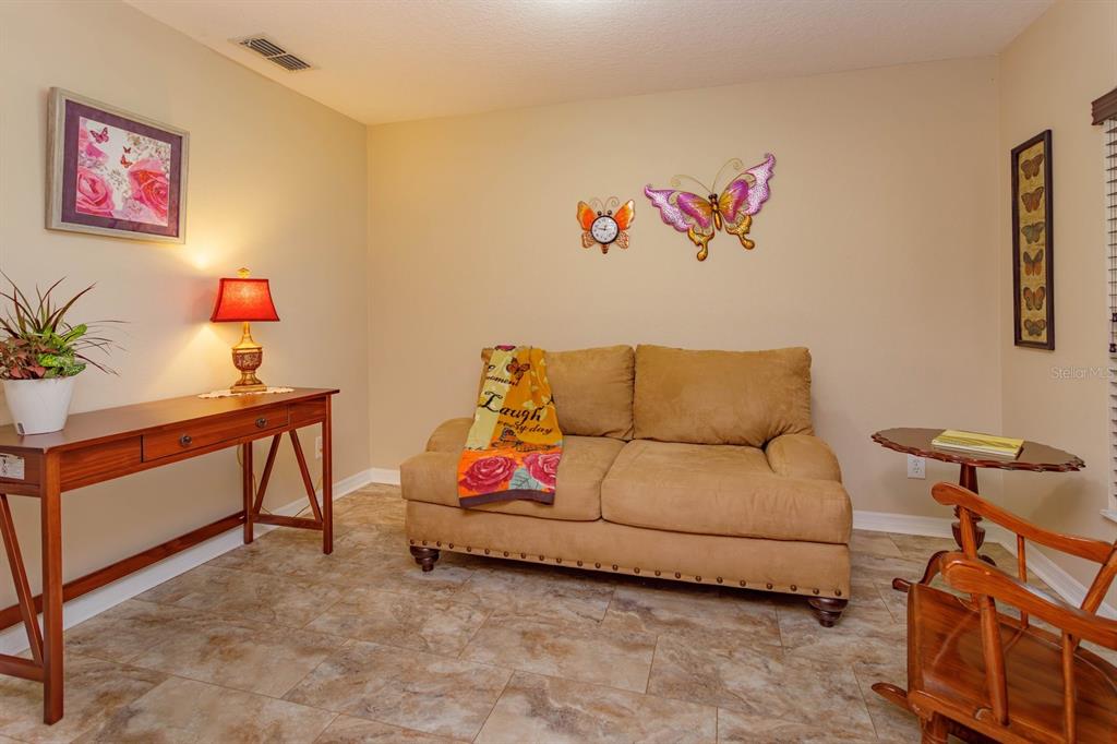 A room with tile flooring, a tan loveseat, a wooden console table, and butterfly wall decor — 24353 CALUSA BOULEVARD, EUSTIS, FL