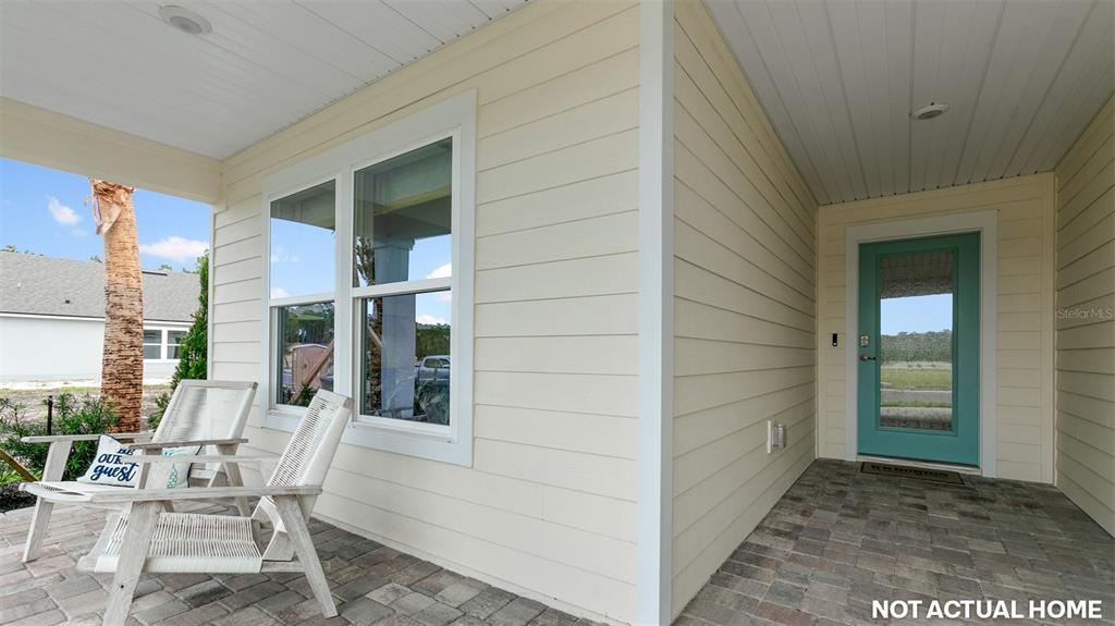 A covered porch with light-colored siding, two chairs, and a teal front door — 59 HARDWOOD TRAIL, PALM COAST, FL