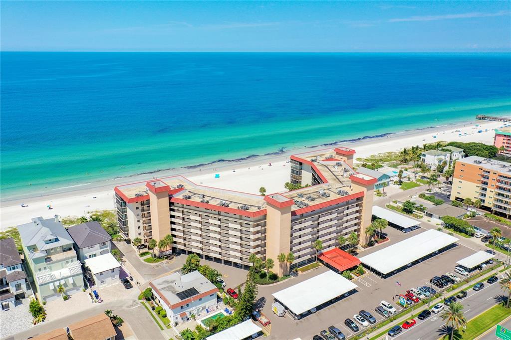 An aerial view shows a multi-story beachfront hotel with a parking lot and sandy beach — 18304 GULF BOULEVARD UNIT 504, REDINGTON SHORES, FL