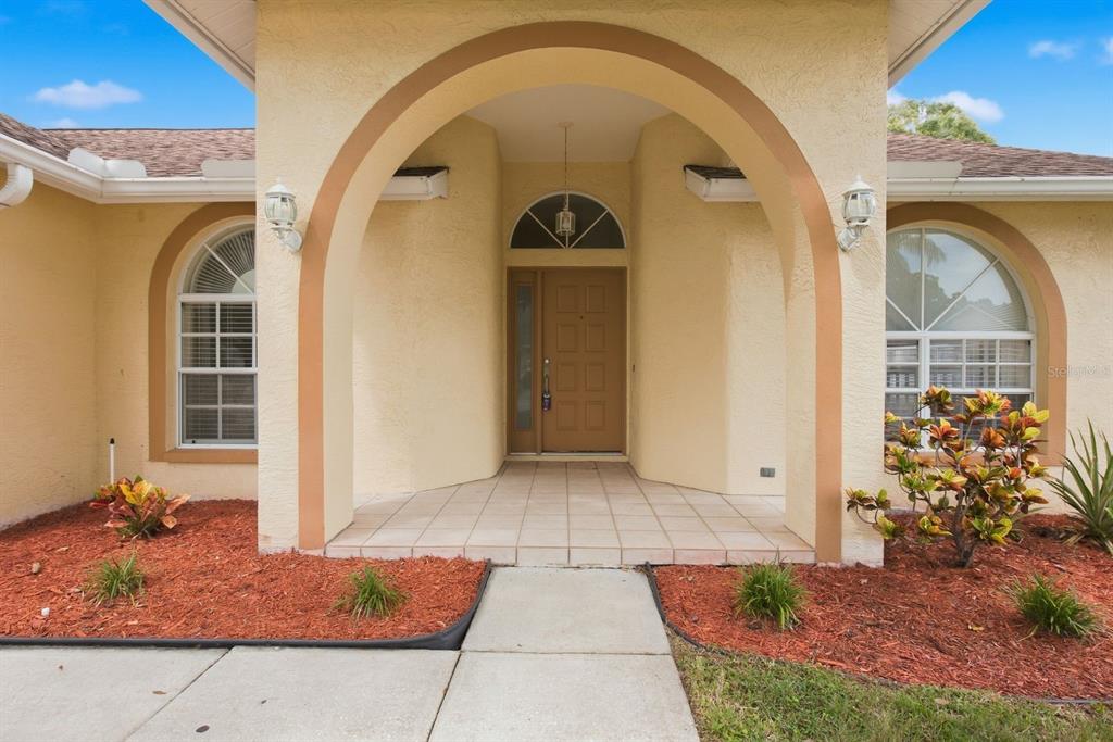 The exterior of a house features a tan arched entryway with a brown front door — 5955 107TH TERRACE N, PINELLAS PARK, FL