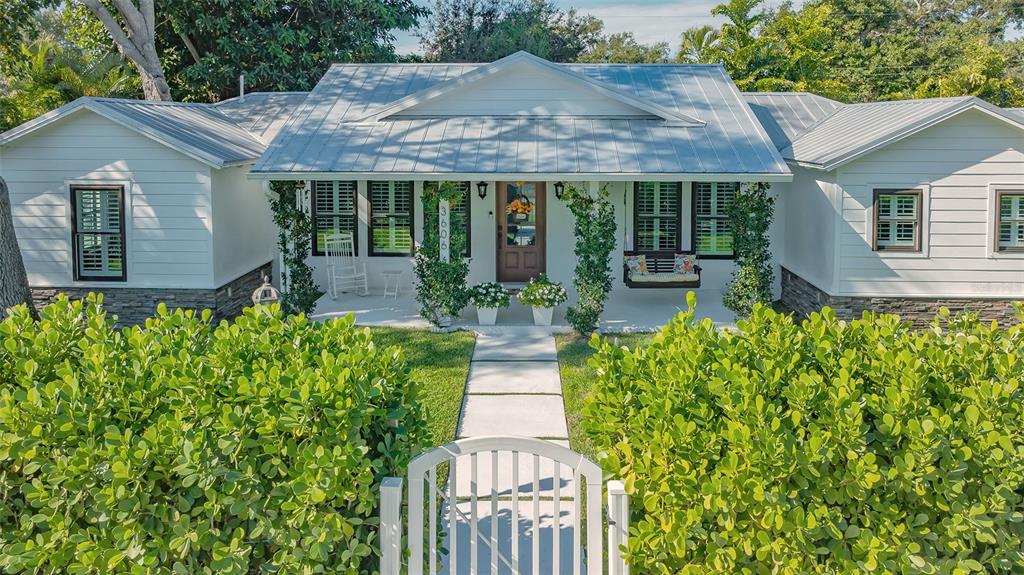 A white house with a metal roof, front porch, and a gated walkway through hedges — 3606 PALONIA COURT, SARASOTA, FL