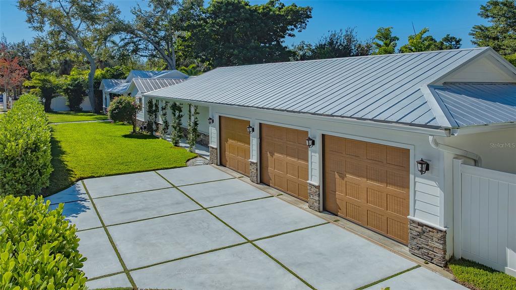 An exterior view shows a three-car garage with a metal roof and concrete driveway — 3606 PALONIA COURT, SARASOTA, FL