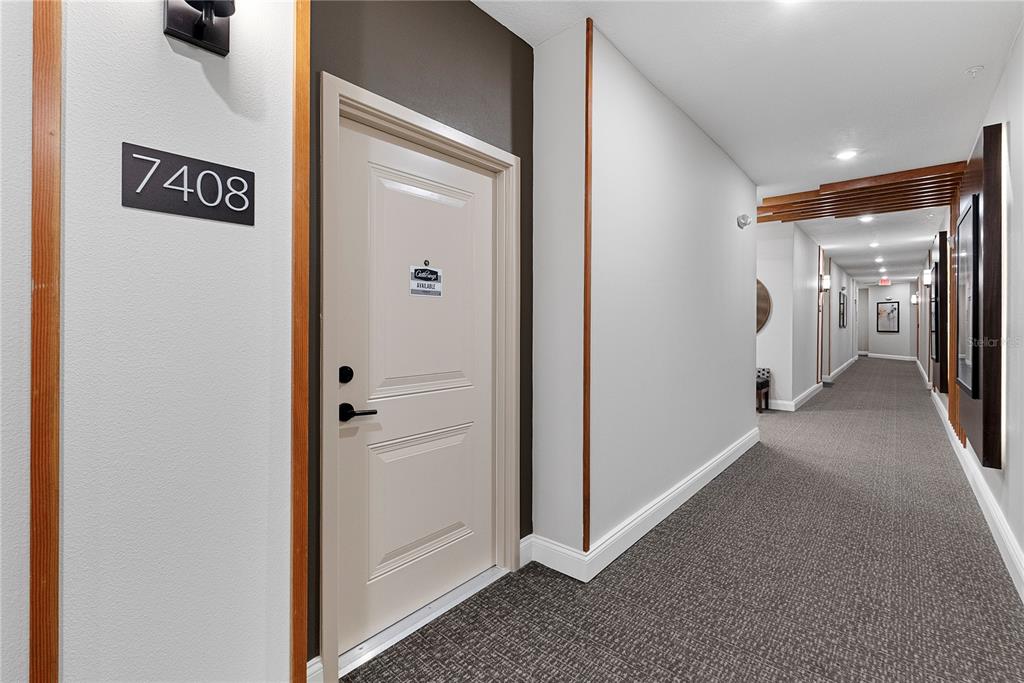 A hallway with gray carpet leads to a beige apartment door labeled 7408 — 7545 LAUREATE BOULEVARD UNIT 7408, ORLANDO, FL