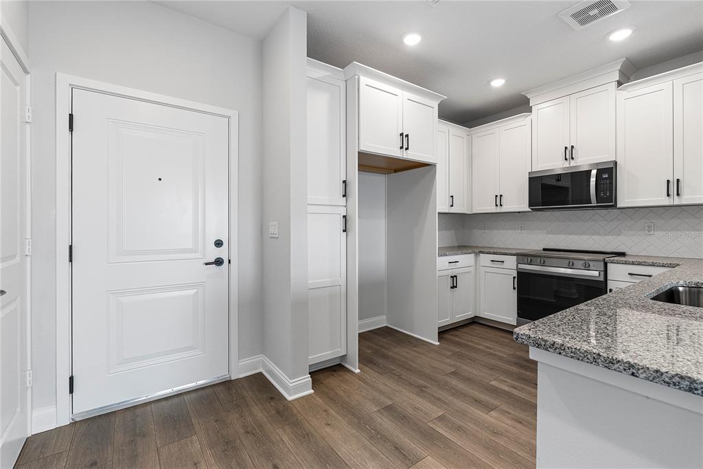 A kitchen features white cabinets, granite countertops, stainless steel appliances, and wood-look flooring — 7545 LAUREATE BOULEVARD UNIT 7408, ORLANDO, FL