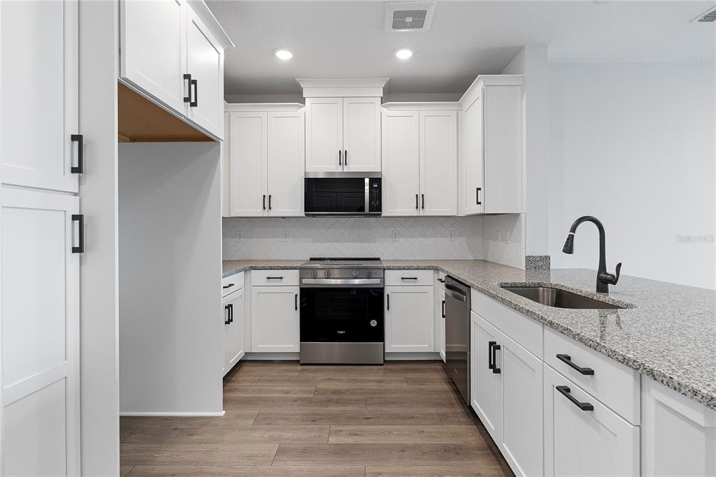 A kitchen with white cabinets, stainless steel appliances, granite countertops, and wood-look flooring — 7545 LAUREATE BOULEVARD UNIT 7408, ORLANDO, FL