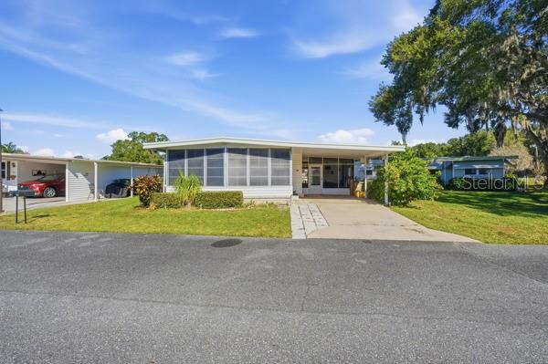A single-story manufactured home with a screened-in front porch and an attached carport — 101 MANGO COVE, LEESBURG, FL