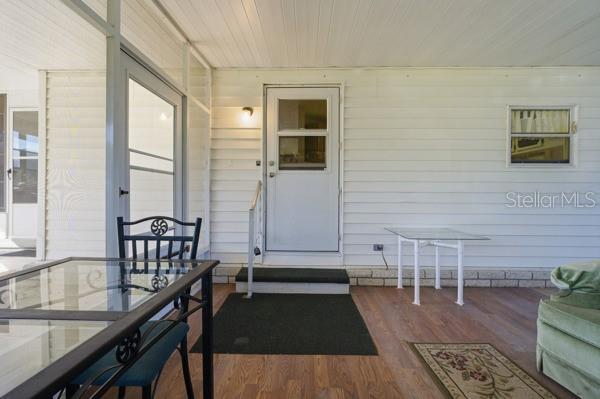 A covered porch features white siding, a glass-paneled door, and a glass-topped dining table — 101 MANGO COVE, LEESBURG, FL