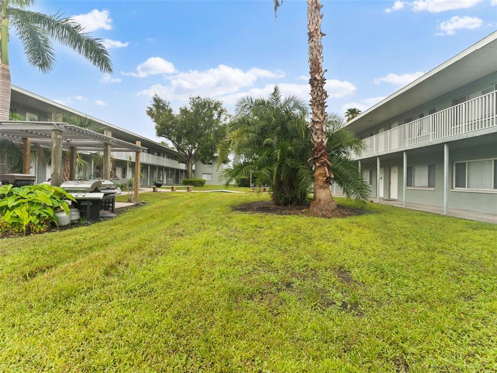 A grassy courtyard sits between two multi-story apartment buildings with palm trees and a grill — 335 47TH AVENUE N UNIT 244, ST PETERSBURG, FL
