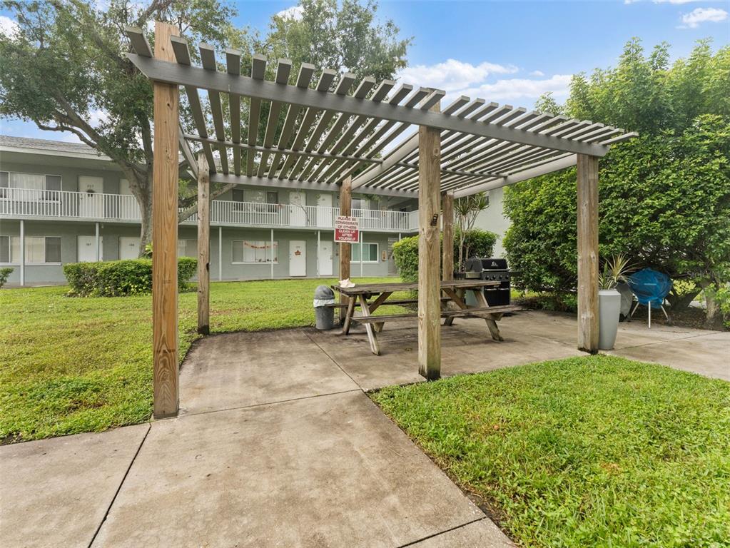 A wooden pergola covers a picnic table and grill on a concrete patio near apartments — 335 47TH AVENUE N UNIT 244, ST PETERSBURG, FL