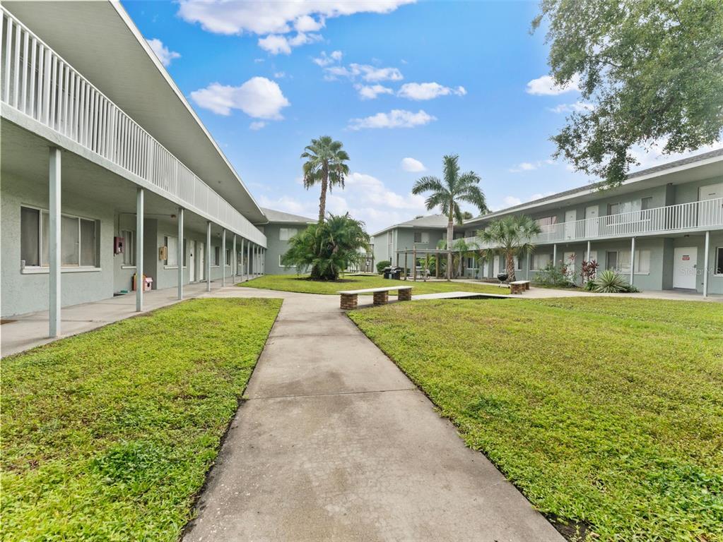 A concrete walkway leads through a grassy courtyard between two-story apartment buildings with balconies — 335 47TH AVENUE N UNIT 244, ST PETERSBURG, FL