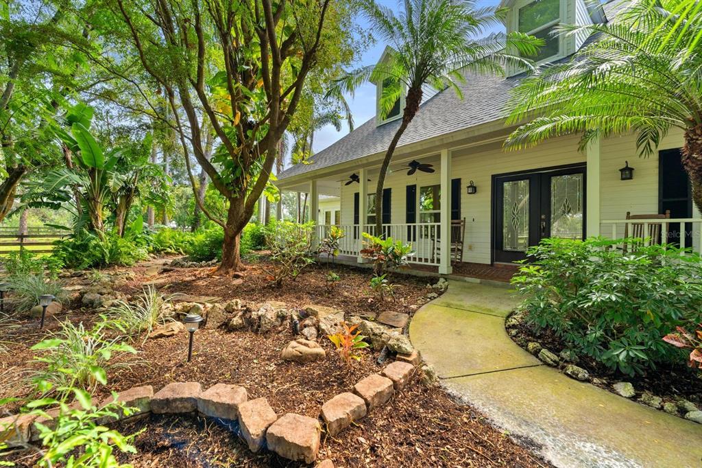 A white house with a covered porch, a curved walkway, and lush landscaping in the yard — 6915 215TH STREET E, BRADENTON, FL