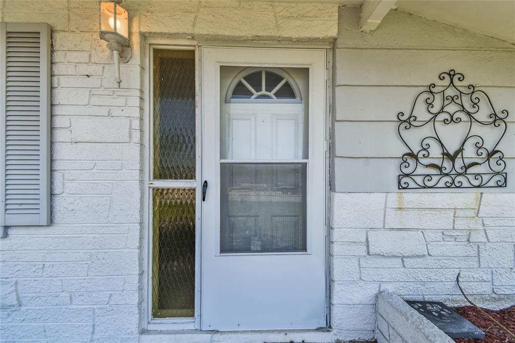 A white front door with a storm door and side light on a stone facade — 13606 ALLYN DRIVE, HUDSON, FL