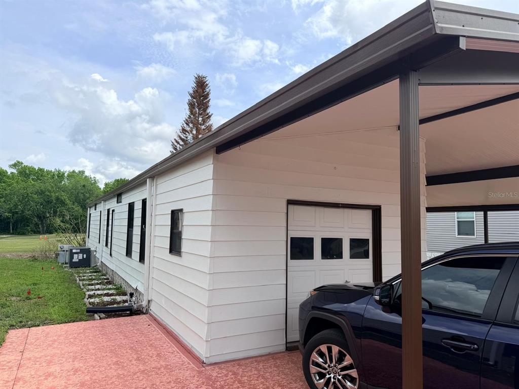 A white mobile home exterior features a carport, a garage door, and a red patio — 2173 PEBBLE BEACH BOULEVARD, ORLANDO, FL