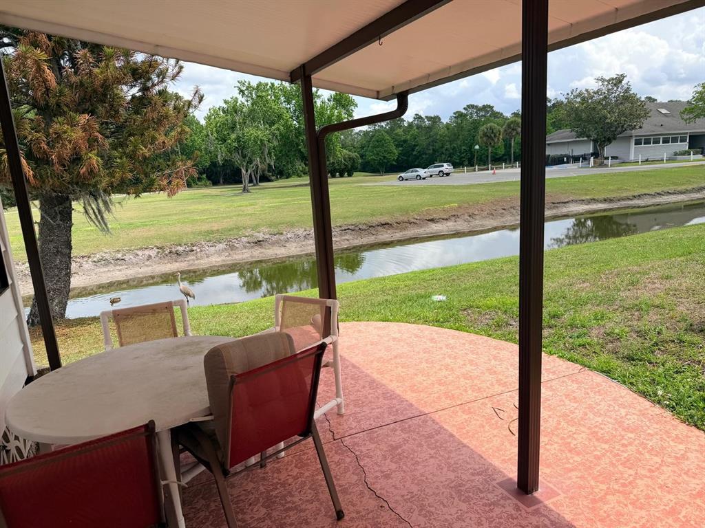 A covered patio with a dining set overlooks a small canal and a grassy field — 2173 PEBBLE BEACH BOULEVARD, ORLANDO, FL