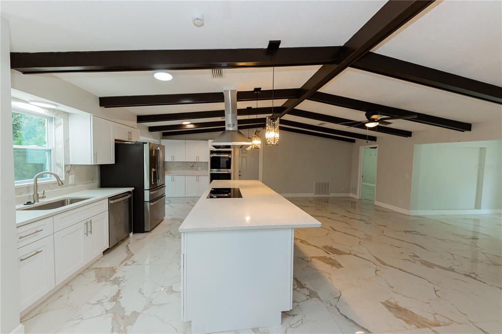 A modern kitchen features white cabinetry, a large island, and dark ceiling beams — 1574 SOUVENIR DRIVE, CLEARWATER, FL