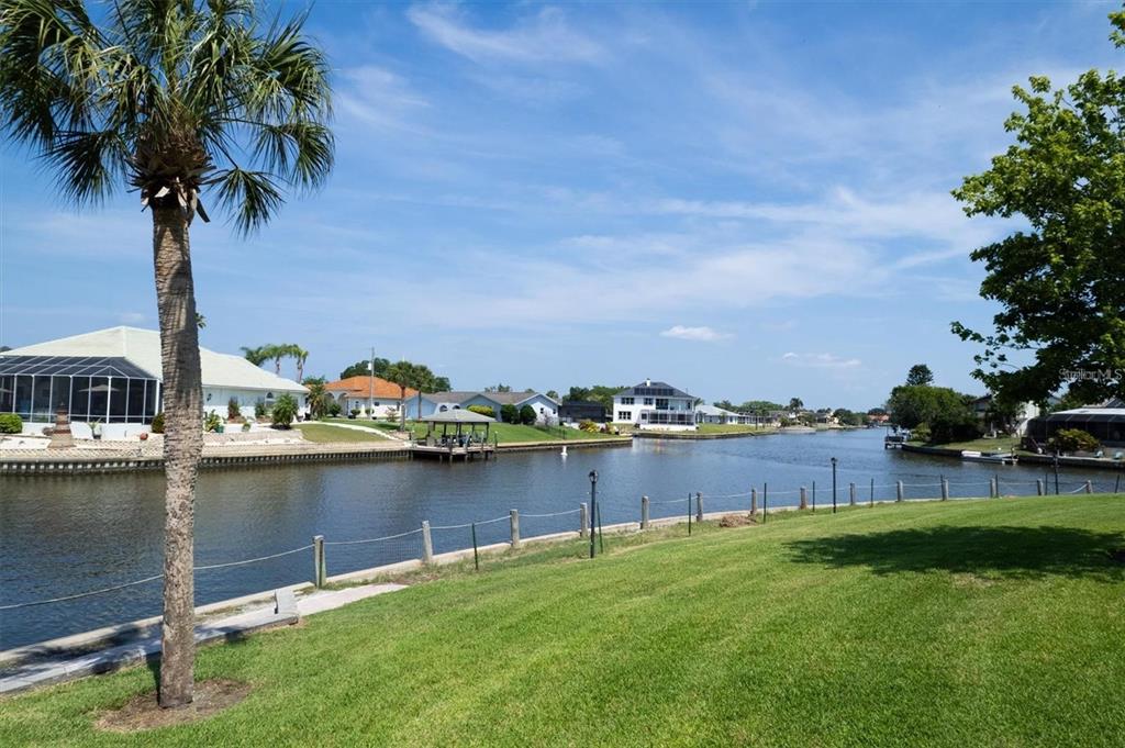 A grassy lawn overlooks a canal lined with houses and a palm tree — 44 CLUB HOUSE DRIVE UNIT 105, PALM COAST, FL