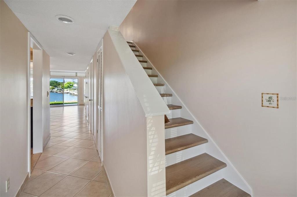 A hallway with tile flooring leads to a waterfront view past a wooden staircase — 44 CLUB HOUSE DRIVE UNIT 105, PALM COAST, FL