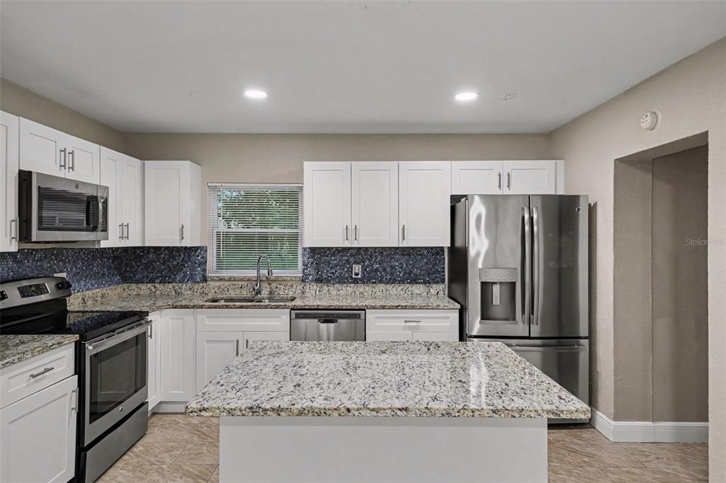 A kitchen features white cabinets, granite countertops, a blue mosaic backsplash, and stainless steel appliances — 1339 E JACKSON AVENUE, MOUNT DORA, FL