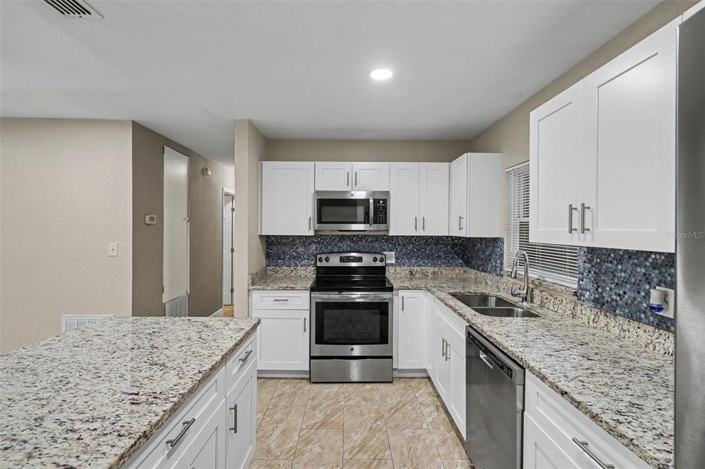A kitchen features white cabinets, granite countertops, stainless steel appliances, and a blue mosaic backsplash — 1339 E JACKSON AVENUE, MOUNT DORA, FL