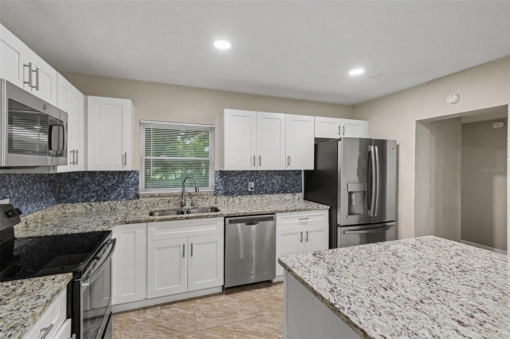 A kitchen features white cabinets, granite countertops, a blue mosaic backsplash, and stainless steel appliances — 1339 E JACKSON AVENUE, MOUNT DORA, FL
