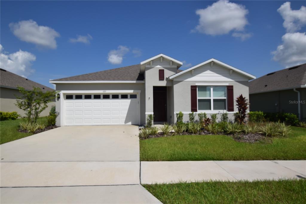 A single-story suburban house with a two-car garage, light stucco exterior, and dark shutters — 5215 MAHOGANY DRIVE, MOUNT DORA, FL