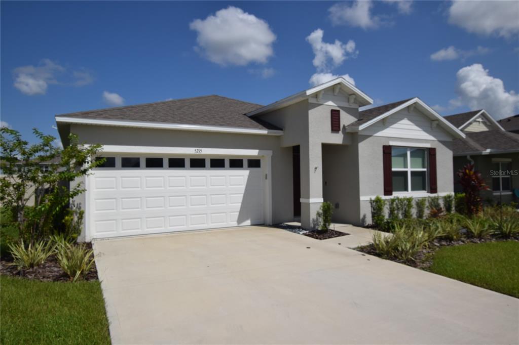 A single-story house with a two-car garage, beige stucco exterior, and a concrete driveway — 5215 MAHOGANY DRIVE, MOUNT DORA, FL