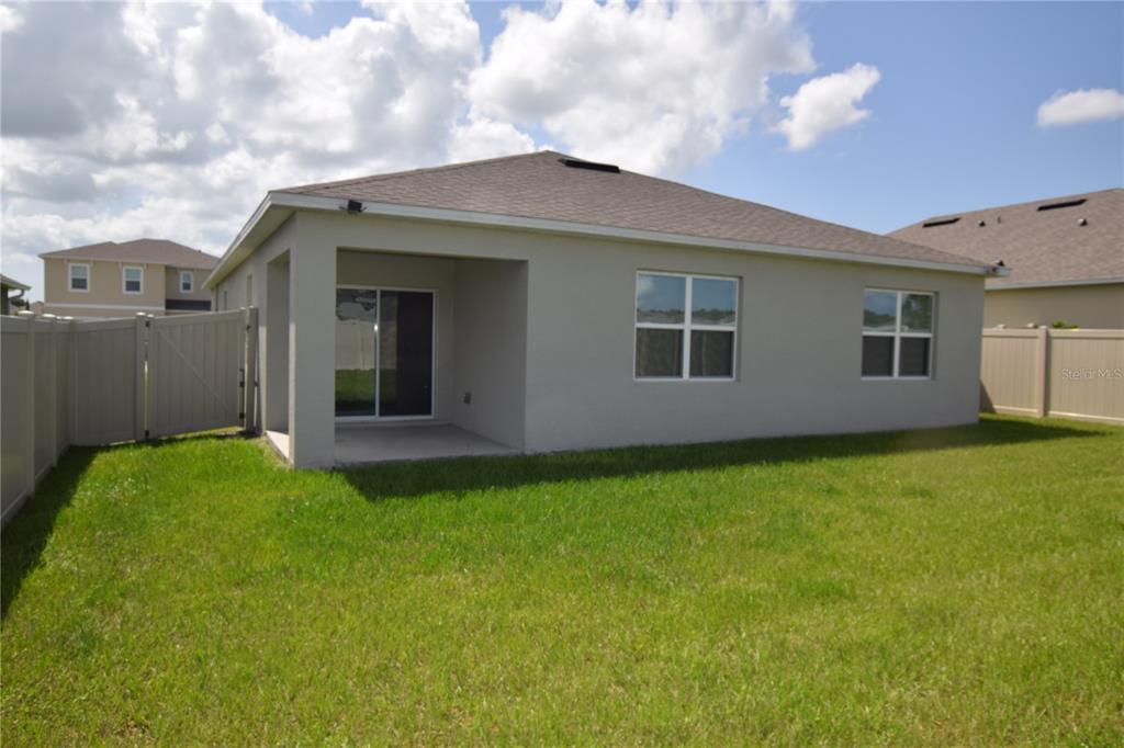 The exterior rear view of a house features a covered patio and a fenced yard — 5215 MAHOGANY DRIVE, MOUNT DORA, FL