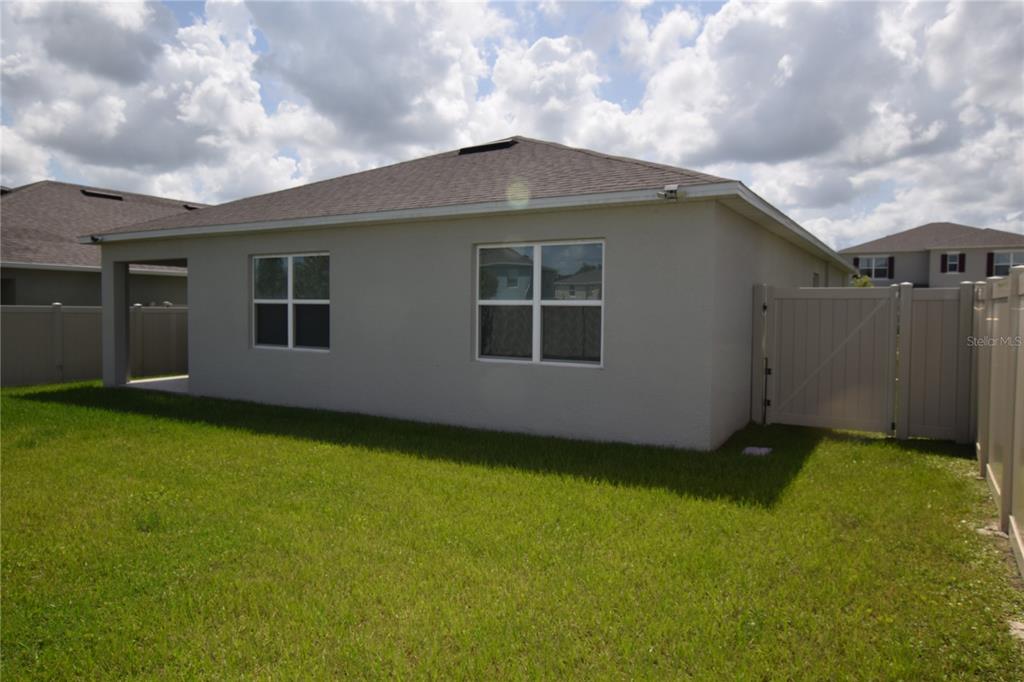 The back exterior of a single-story house features a tan stucco wall, two windows, and a fence — 5215 MAHOGANY DRIVE, MOUNT DORA, FL