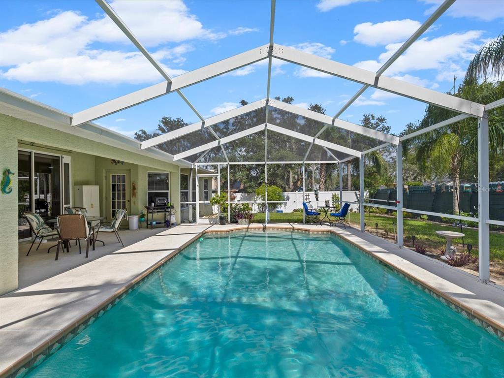 A rectangular swimming pool sits inside a screened-in lanai attached to a light green house — 5733 CACTUS CIRCLE, SPRING HILL, FL