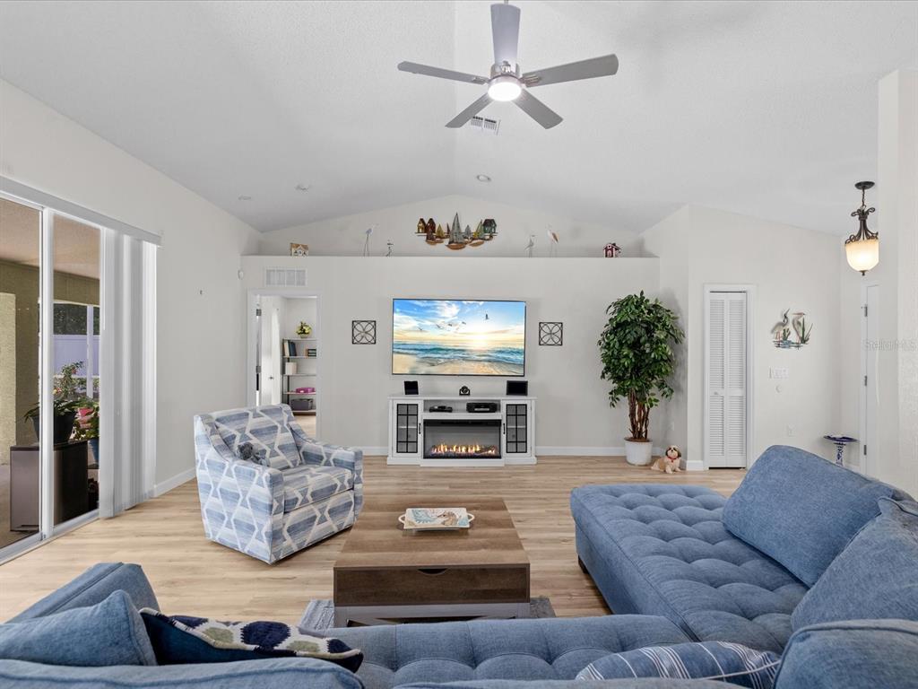A living room features a blue sectional sofa, patterned armchair, television, and fireplace console — 5733 CACTUS CIRCLE, SPRING HILL, FL