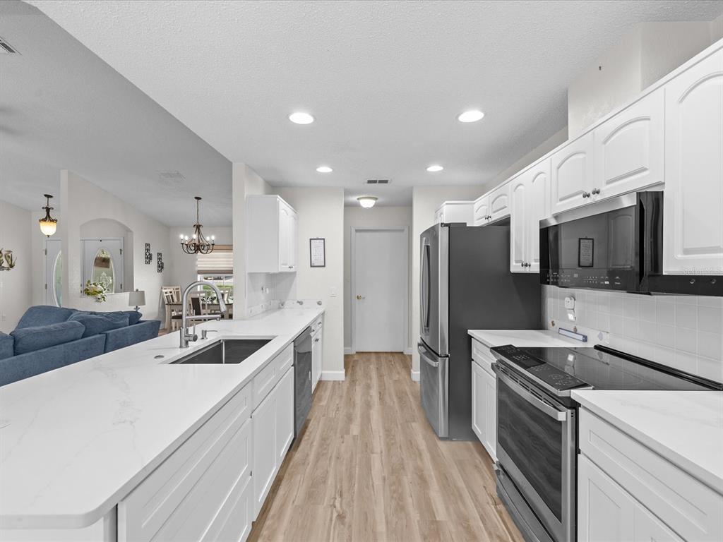A modern kitchen features white cabinets, quartz countertops, stainless steel appliances, and light wood flooring — 5733 CACTUS CIRCLE, SPRING HILL, FL