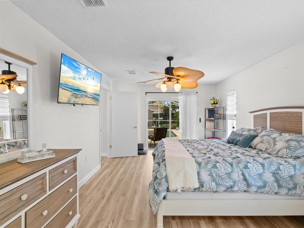 A bedroom features a bed with palm-print bedding, a wood dresser, and a ceiling fan — 5733 CACTUS CIRCLE, SPRING HILL, FL