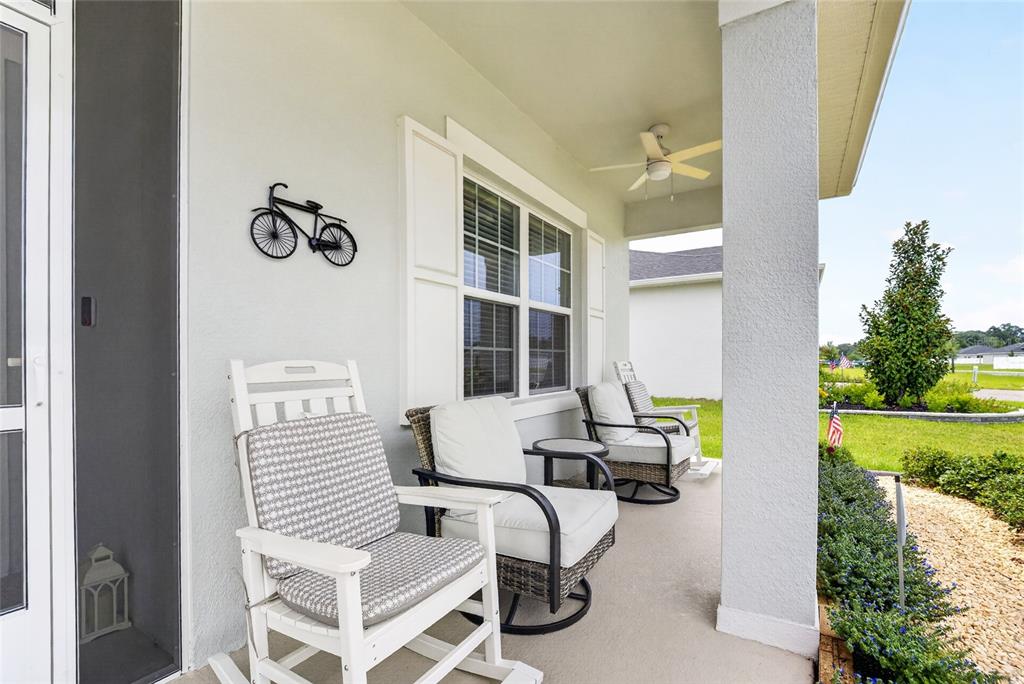 A covered front porch features three outdoor chairs, a ceiling fan, and a bicycle wall decoration — 10859 SW 72ND CIRCLE, OCALA, FL