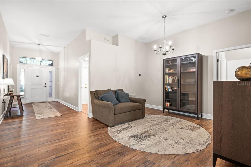 A foyer features wood-look flooring, a brown armchair, a glass-front cabinet, and a chandelier — 14432 BARLEY FIELD DRIVE, WIMAUMA, FL
