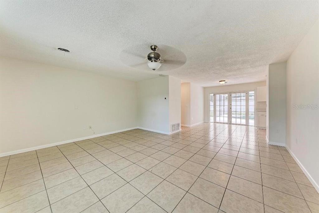 An open-concept living area features light-colored tile flooring, a ceiling fan, and glass sliding doors — 3207 19TH AVENUE W, BRADENTON, FL